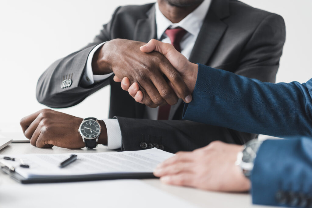 cropped shot of multicultural businessmen shaking hands during contract signing at workplace